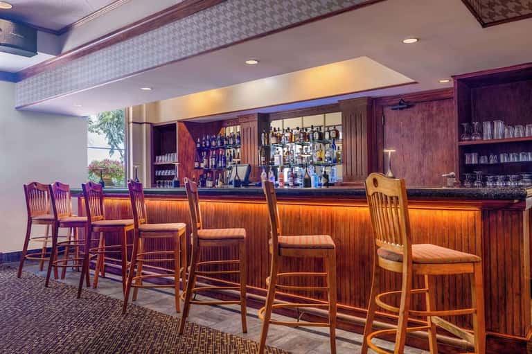 Hotel bar with wooden paneling, bar stools, and illuminated shelves of liquor bottles