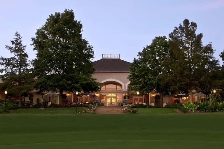 Elegant estate building at dusk with manicured lawn, arched entrance, and landscape lighting