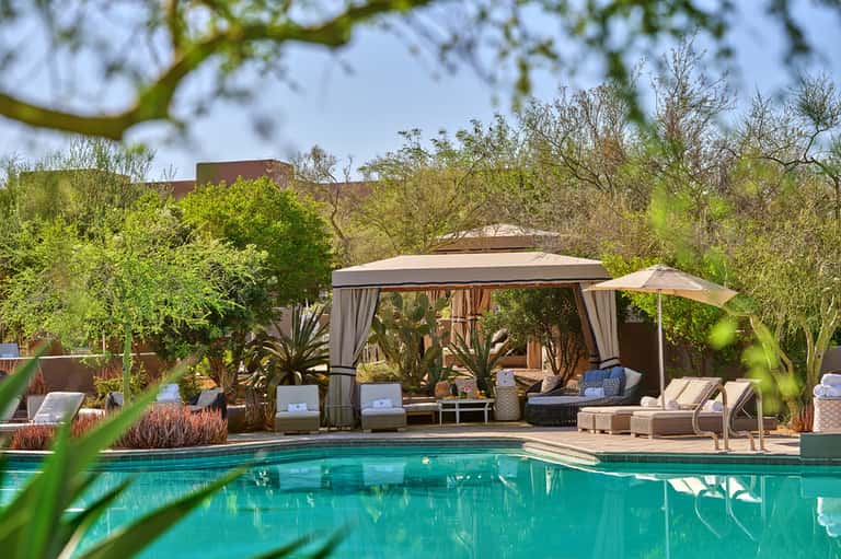 Luxury pool cabana with white curtains, loungers, and desert landscape views