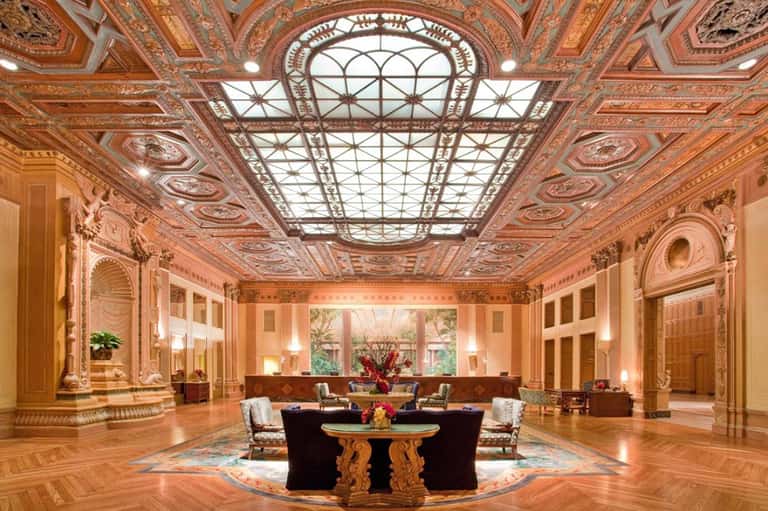 Grand ornate ballroom with decorative ceiling, skylight, marble floors, and central furniture arrangement
