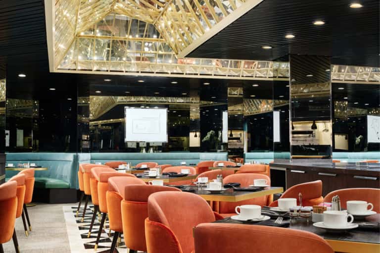 Modern hotel dining room with orange curved chairs, black tables, and large windows