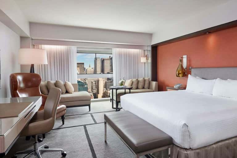 Luxury hotel suite with city skyline view, king bed, lounge seating, and orange accent wall