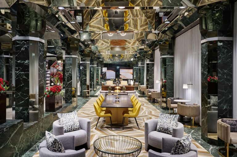 Luxurious modern lobby with marble columns, golden ceiling details, yellow chairs, and geometric flooring