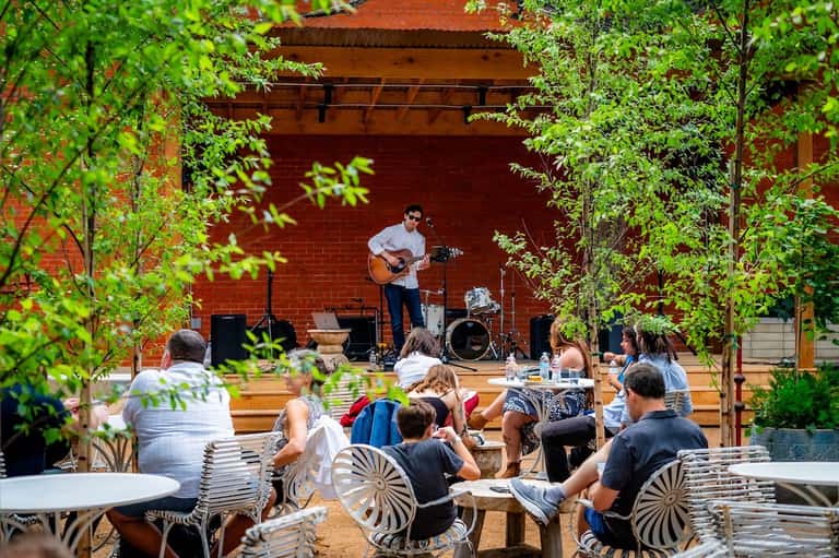 Live musician performing guitar for outdoor audience under red brick building