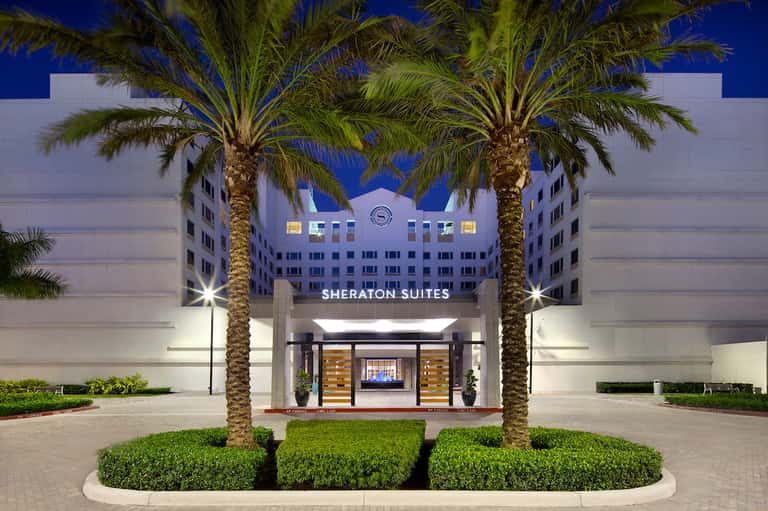 Sheraton Suites entrance with white modern facade, palm trees flanking sides, and lit signage at night