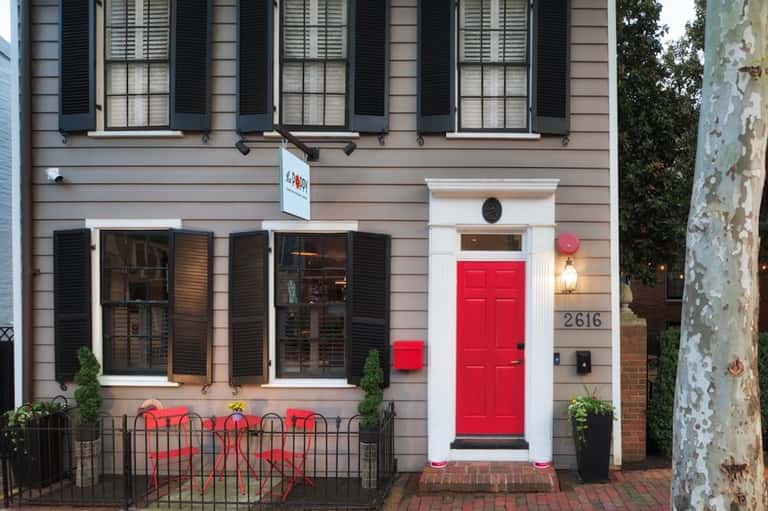 Historic charming storefront with red door, black shutters, large windows, and brick facade