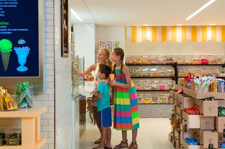 Colorful ice cream parlor with family ordering at counter, bright yellow striped ceiling, candy displays