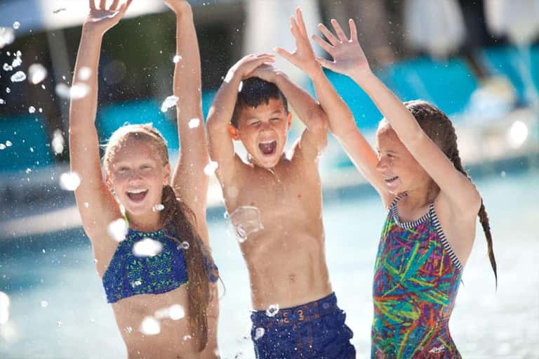 Children playing and splashing in resort pool with blue umbrellas