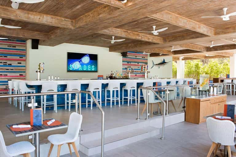 Modern beachfront bar with blue bar stools, exposed wooden beams, and colorful nautical wall decor
