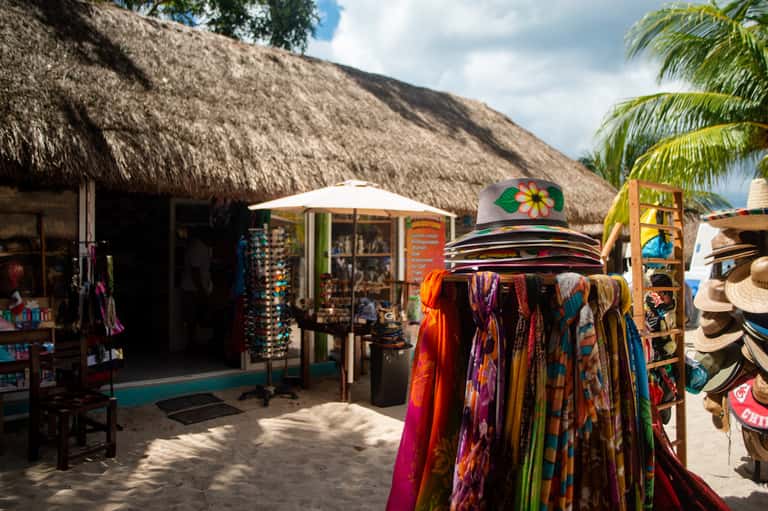 Beach market stall with colorful clothing, hats, and souvenirs displayed under thatched roof