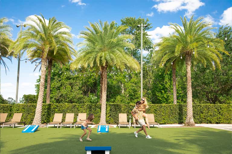 Manicured lawn with tall palm trees, lounge chairs, and two people playing cornhole