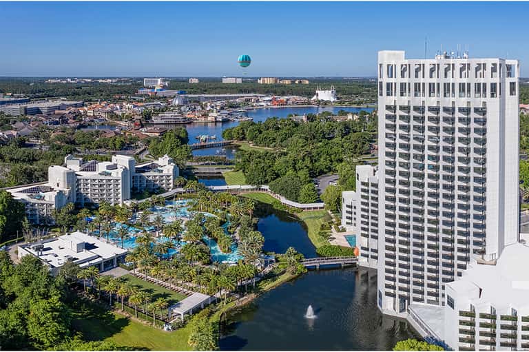 Aerial resort view with pools, palm trees, white buildings, and theme park in background