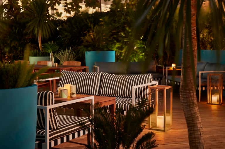 Outdoor lounge area at night with striped seating, potted plants, and ambient lighting