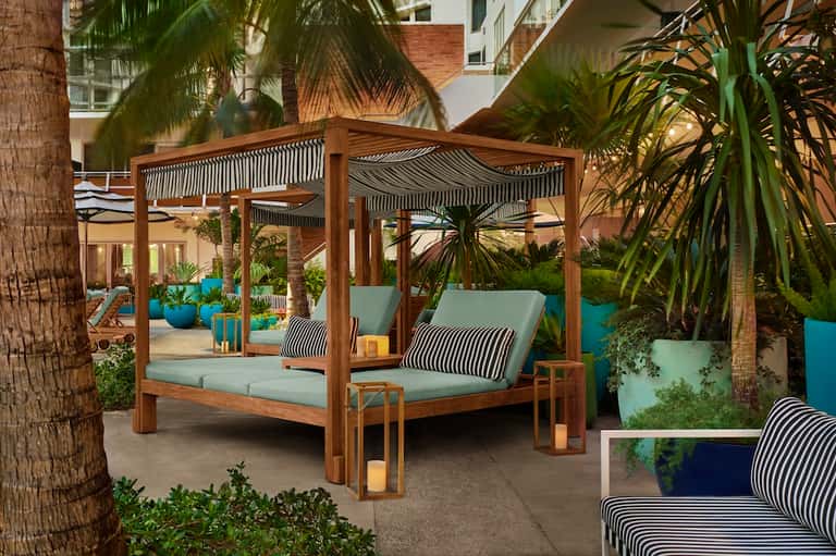 Wooden pergola daybed with turquoise cushions and striped pillows in tropical courtyard setting