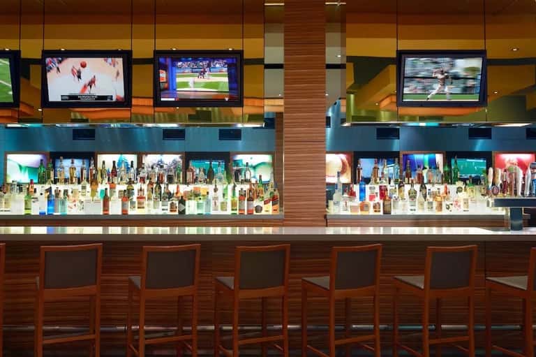 Sports bar with multiple TV screens and illuminated liquor display behind counter