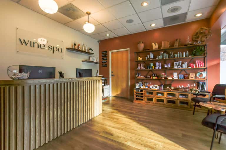 Wine spa reception desk with wooden counter, orange accent walls, and shelving displaying products