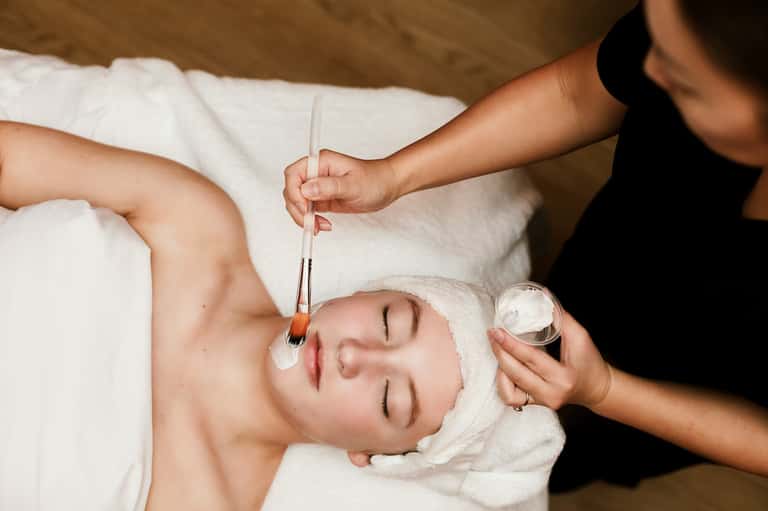 Spa therapist applying facial treatment to relaxed client in white towel