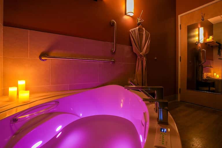 Luxurious spa bathroom with magenta-lit soaking tub, amber wall tiles, and mood lighting