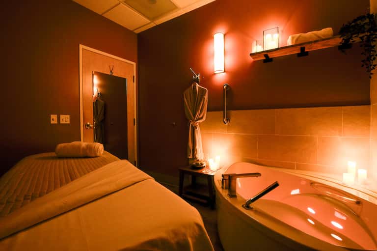 Spa treatment room with massage bed, soaking tub, and warm orange lighting