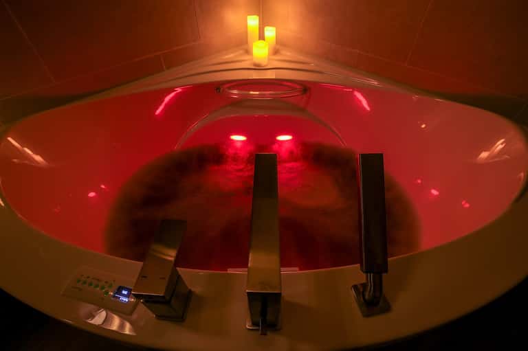 Modern spa soaking tub with red light therapy illumination and candles for relaxation
