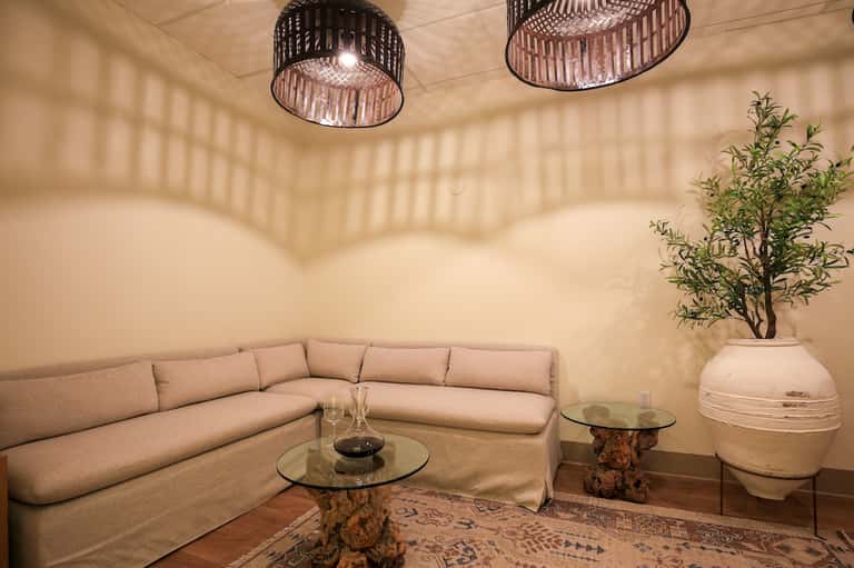 Modern spa lounge with beige sectional sofa, decorative pendant lights, and potted plant