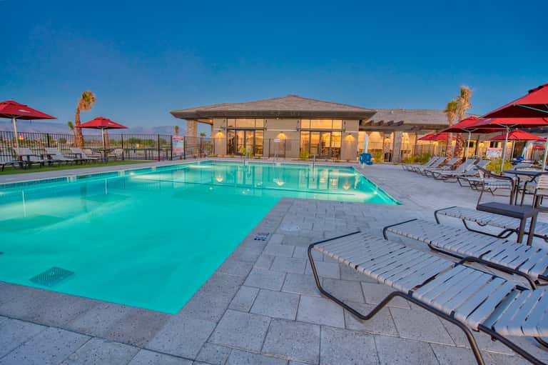Resort outdoor pool at dusk with red umbrellas, lounge chairs, and mountain views