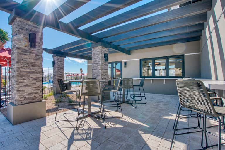 Modern patio with pergola, stone columns, bar seating, and pool view in background