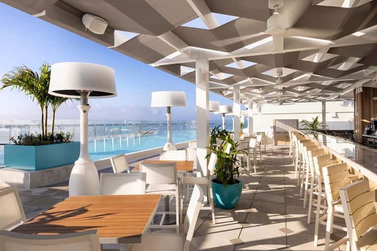 Rooftop restaurant terrace with pool view, white pergola, and casual dining setup
