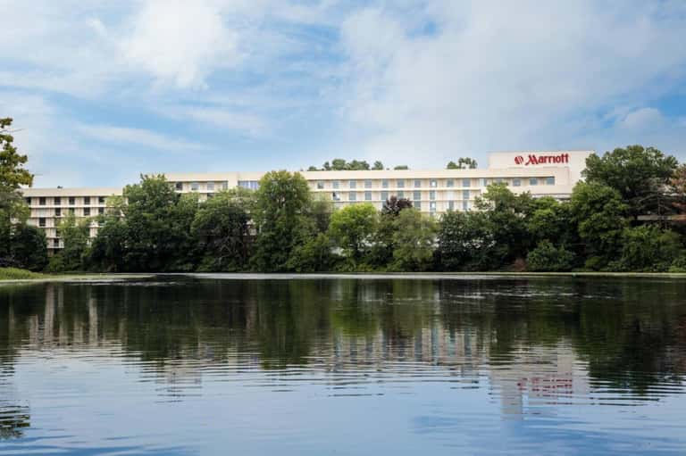 Marriott hotel exterior reflected in calm river water surrounded by green trees