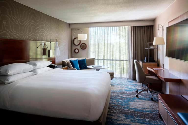 Contemporary hotel room with king bed, work desk, seating area, and floor-to-ceiling windows with ocean views