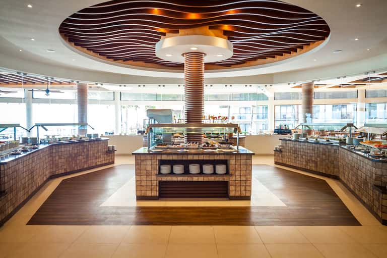Modern hotel dining area with sculptural wooden ceiling feature and open kitchen concept