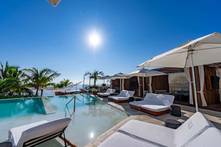 Luxury resort pool terrace with turquoise water, white lounge chairs, umbrellas, and ocean backdrop