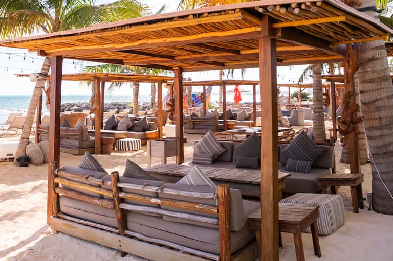 Beachfront cabanas with wooden pergolas, striped cushions, and ocean view under palm trees