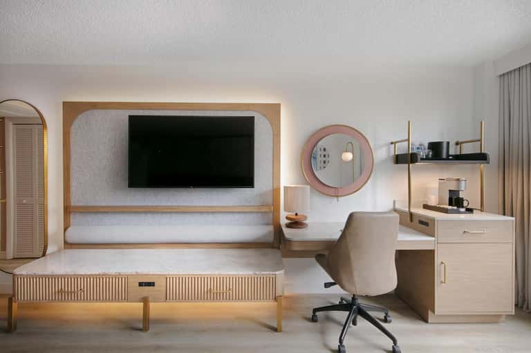 Modern hotel room with wooden bed frame, TV with surround, desk chair, and contemporary furnishings