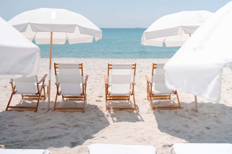 Beach cabanas with white umbrellas and wooden loungers facing turquoise ocean