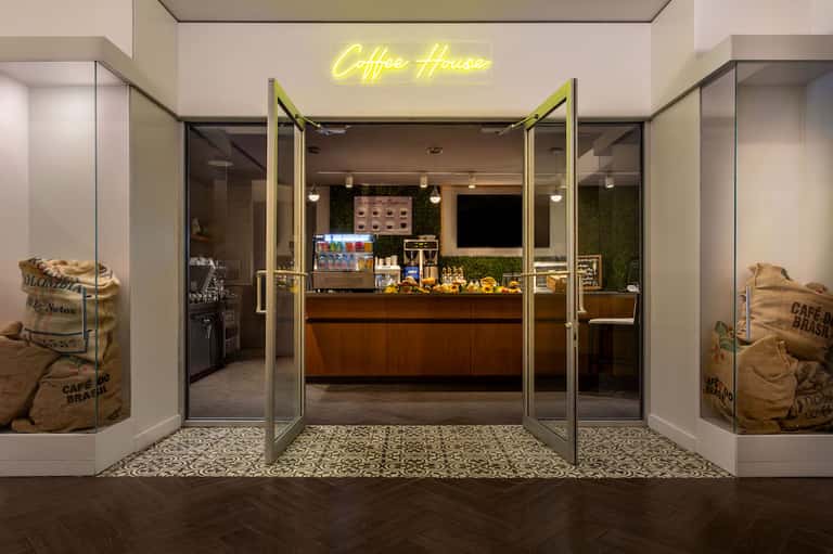 Coffee house entrance with neon sign, glass doors, wooden counter, and decorative coffee bean displays