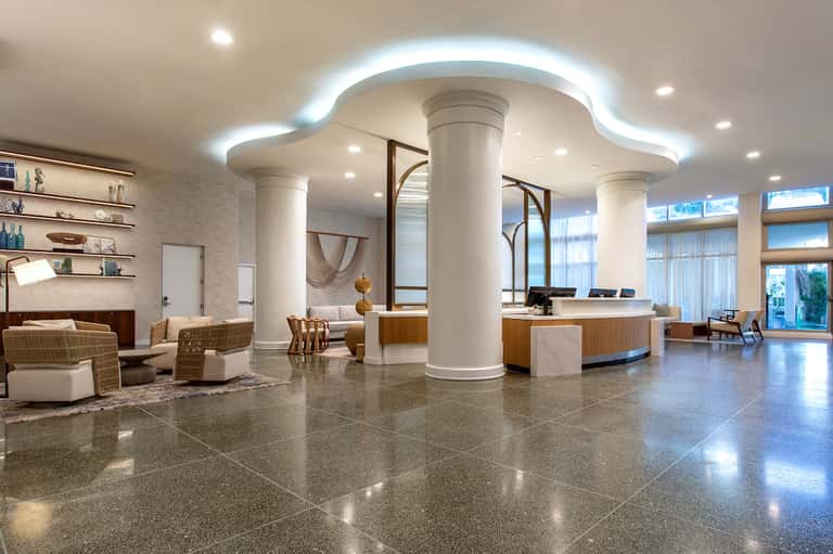 Modern hotel lobby with polished terrazzo floors, white columns, curved ceiling with LED lighting, and wooden reception desk