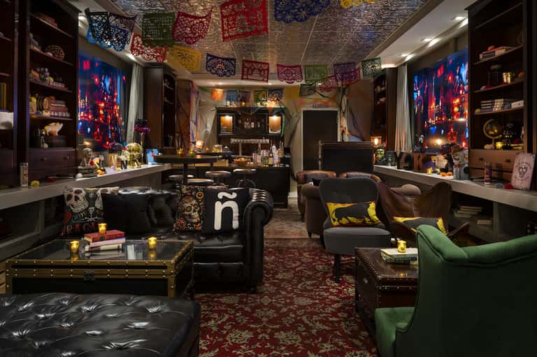 Eclectic lounge with dark furniture, colorful pendant decorations, neon artwork, and ornate shelving