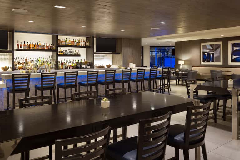 Modern hotel bar and lounge with black chairs, blue cushions, and extensive liquor selection