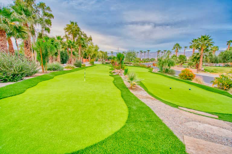 Mini golf course with bright green fairways, palm trees, and desert mountains in background