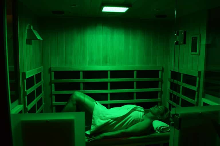 Person lying in infrared sauna with green light therapy and wooden benches