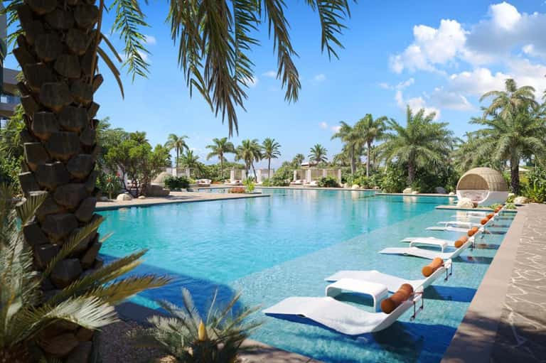 Resort pool with turquoise water, palm trees, loungers, and sunny skies