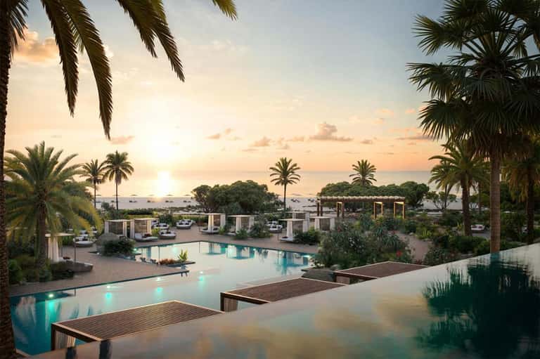 Luxury beachfront resort at sunset with illuminated pool, palm trees, and ocean view