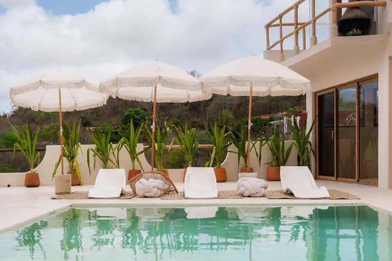 Resort pool area with white umbrellas, lounge chairs, and modern architectural building