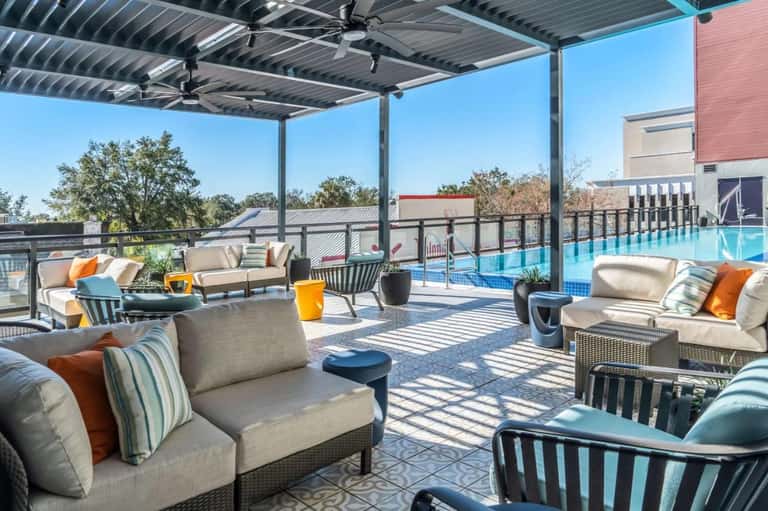 Rooftop pool deck with lounge seating, pergola shade structure, and resort buildings in background