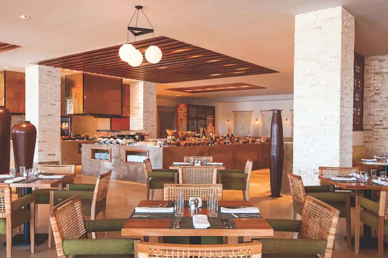 Upscale dining room with brick columns, woven chairs, warm lighting, and modern bar area