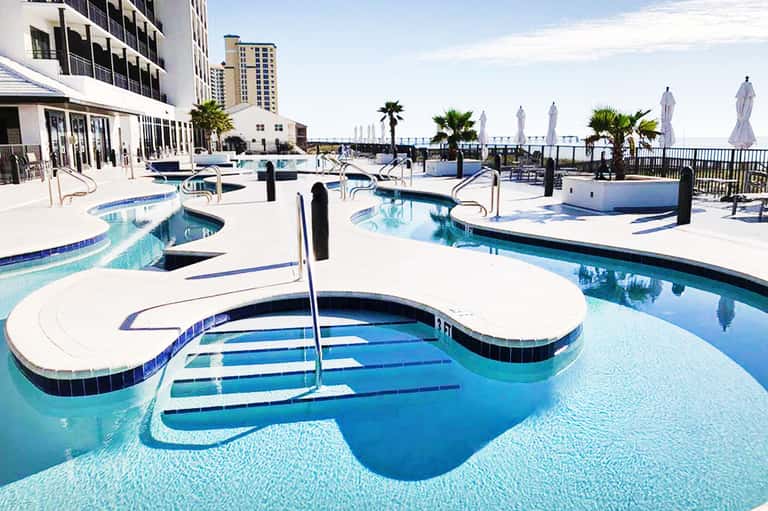Rooftop pool deck with multiple pools, umbrellas, ocean view, and high-rise hotel building