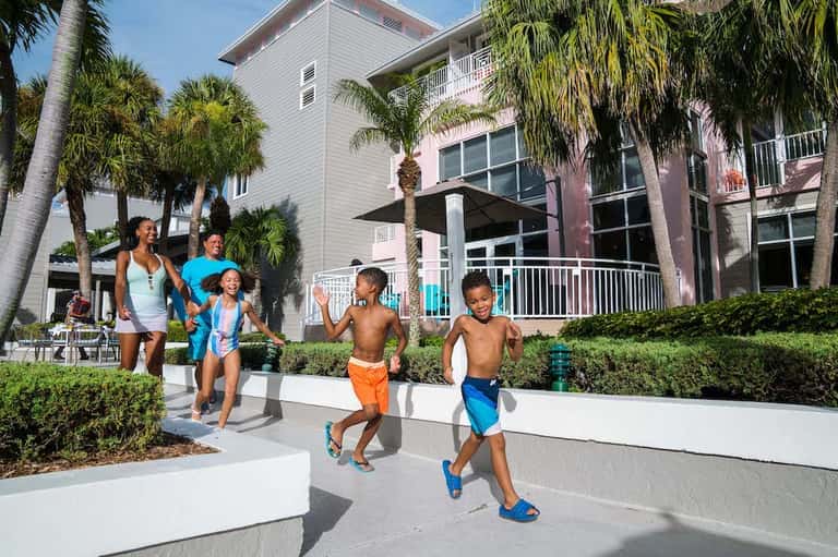 Family jogging on white pathway between modern beach houses with palm trees