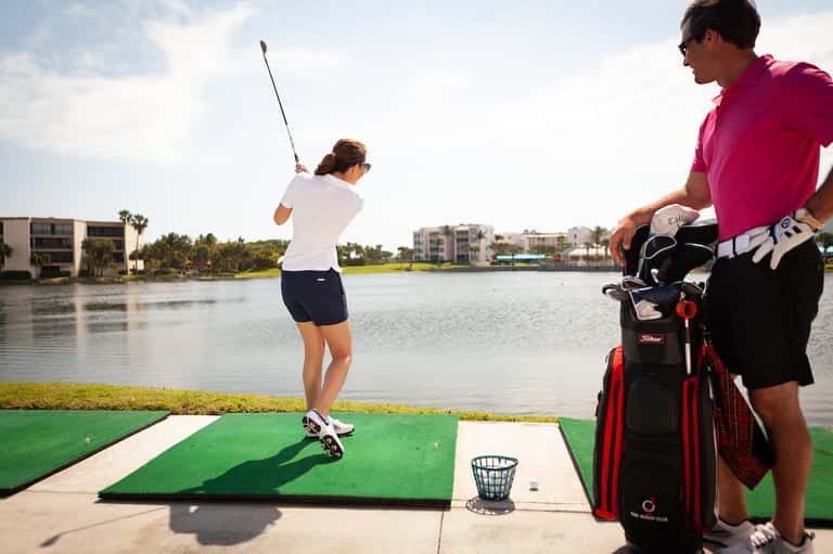 Golfer taking a swing at driving range overlooking waterfront property