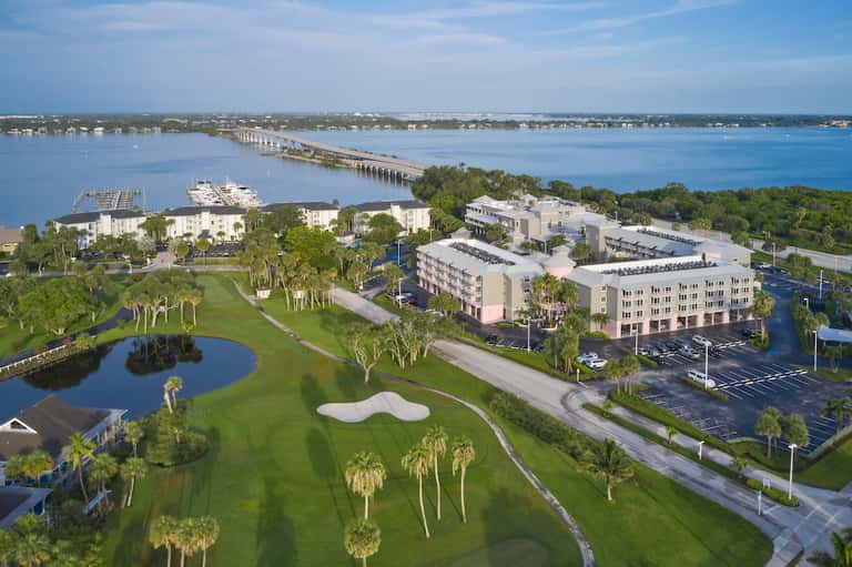 Aerial view of beachfront resort with buildings, golf course, pools, and waterway at sunset
